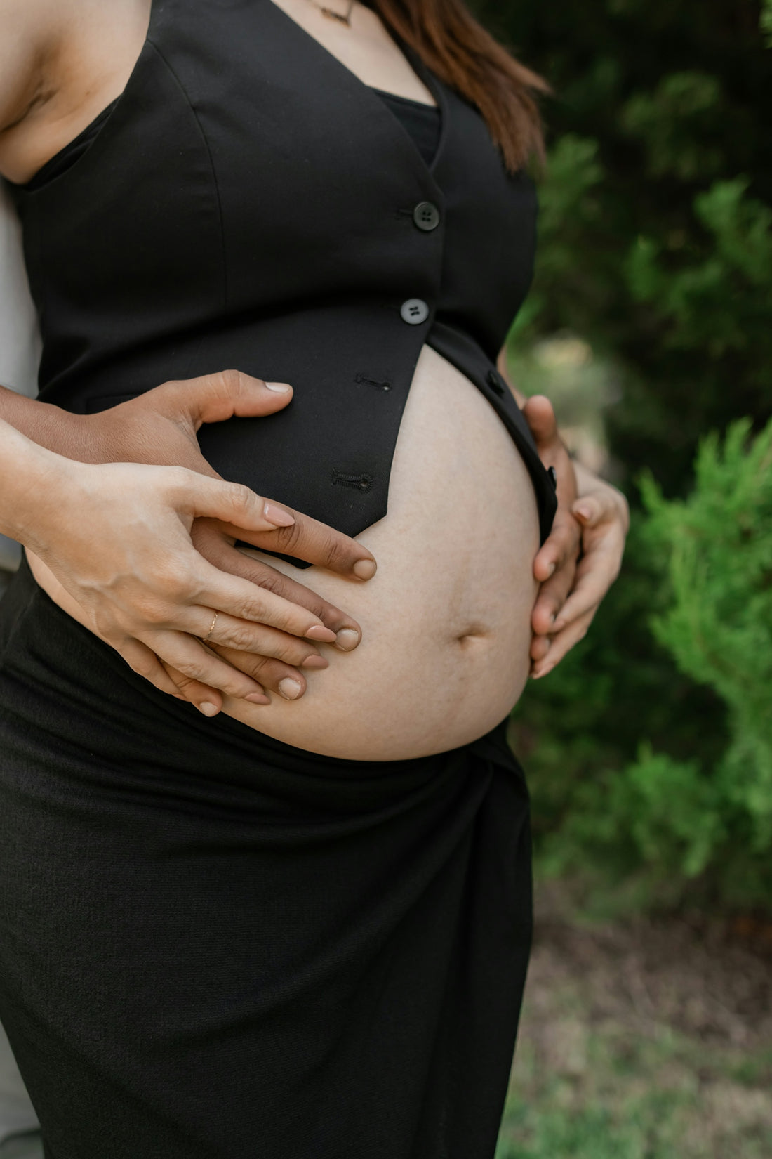 A pregnant woman in a black dress holding her belly