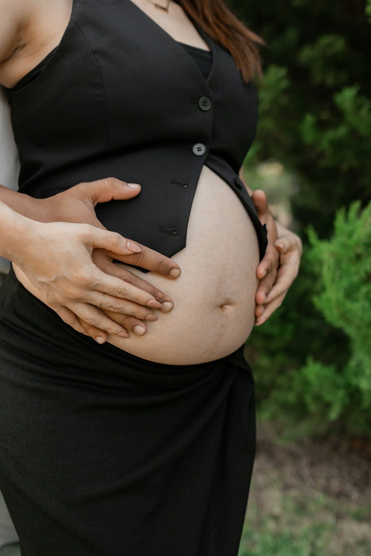 A pregnant woman in a black dress holding her belly